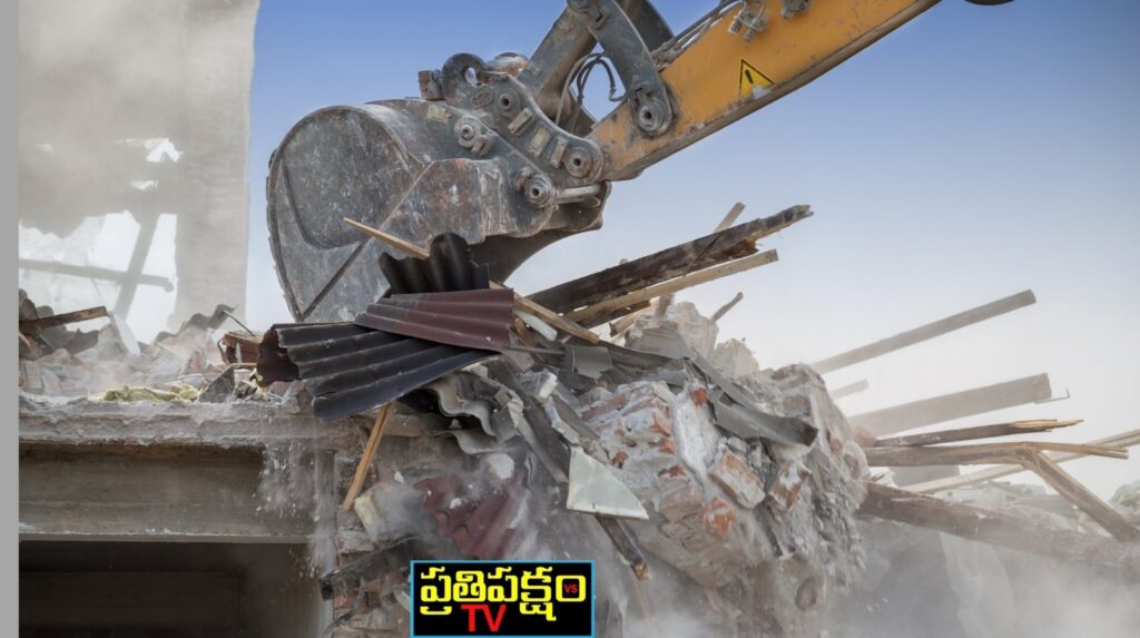 “Excavator demolishing a damaged building with debris and dust in the air – Prathipaksham TV.”